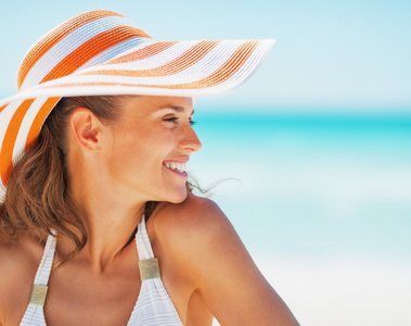 泳装和海滩的帽子看起来幸福的年轻女人的画像