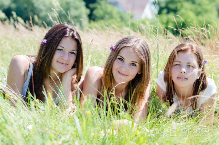 躺在高高的绿草丛中的三个快乐青少年女孩朋友
