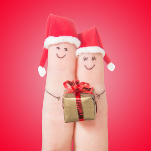 在圣诞老人的帽子与礼品盒的手指脸。对幸福的夫妇的概念