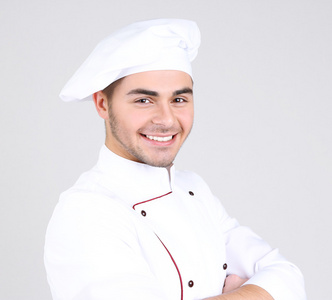 专业的厨师，在白色的制服和帽子，在灰色的背景上