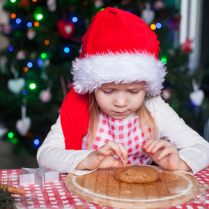 可爱的小女孩，在圣诞老人的帽子吃生姜饼干面团