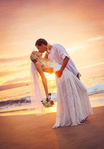 新郎和新娘，在美丽的热带海滩在日落时接吻