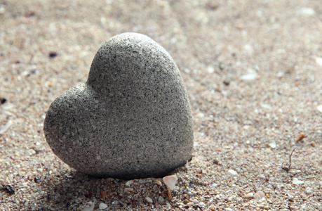 恨石灰色的石头在心,砂背景上的形状摄影图