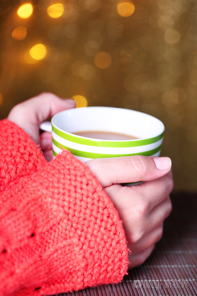 手里捧着大杯热饮料特写在明亮的背景上