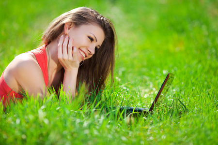 一个聪明的年轻女人躺在草地上，使用笔记本电脑的肖像