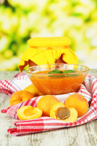 杏酱在玻璃碗和新鲜的杏子，木桌上，在明亮的背景上