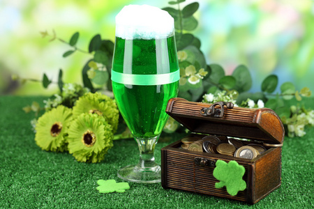 绿色的啤酒和投手与硬币上草特写的玻璃