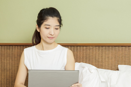 使用笔记本电脑在卧室里的快乐年轻亚裔女子