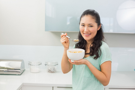 微笑的年轻女人，在厨房里吃谷类食品