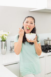 一个年轻的女人，在厨房里吃沙拉的肖像