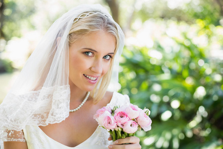 幸福的新娘，抱着她的花束看看相机的面纱