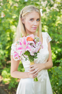 金发碧眼的新娘紧握着大束鲜花，在相机微笑
