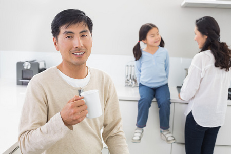 拿着咖啡杯子与家庭背景的男人微笑着