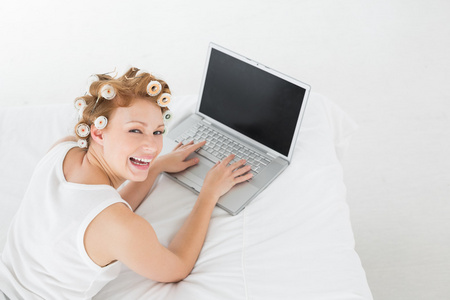 性格开朗的女人在卷发在床上使用笔记本电脑