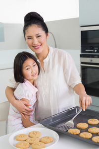 母亲拥抱女儿在厨房里的饼干在准备的时候