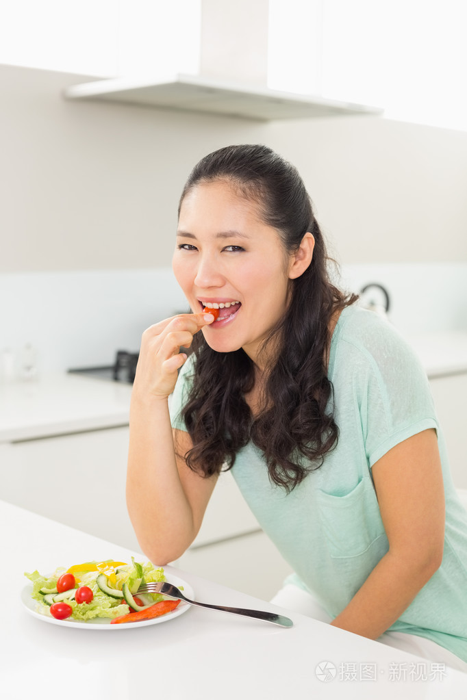 一个年轻的女人，在厨房里吃沙拉的肖像
