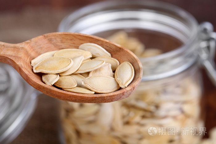 graines de citrouille dans la cuillre et jar sur table bouchent