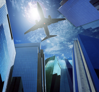 客机飞越现代办公大楼反对蓝蓝的天空白云似乎城市生活和空中运输业务场景