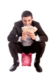 愉快的商业人坐在小猪银行数钱欧元
