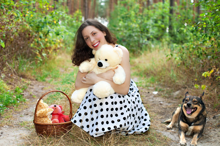 漂亮的女孩，与狗和玩具熊坐在木头