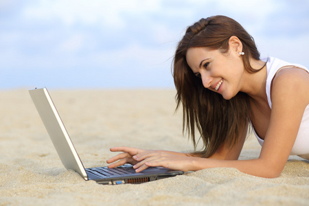 浏览她的笔记本电脑，躺在沙滩上一个十几岁女孩的侧视图