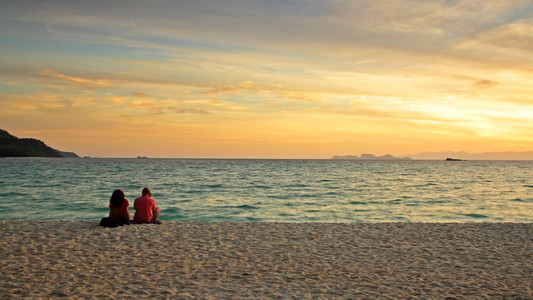夫妻坐在沙滩上享受日出时分敦利普