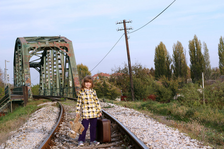 手提箱和泰迪熊站在铁路上的小女孩
