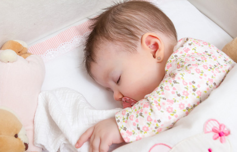宝贝女孩睡在一张小床与婴儿奶嘴和玩具