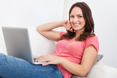 女人坐在沙发上使用的便携式计算机