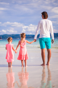 在白色的热带海滩后视图的两个小女孩和年轻的父亲