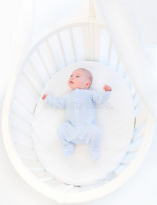 可爱的新生男婴在白色的圆形婴儿床上