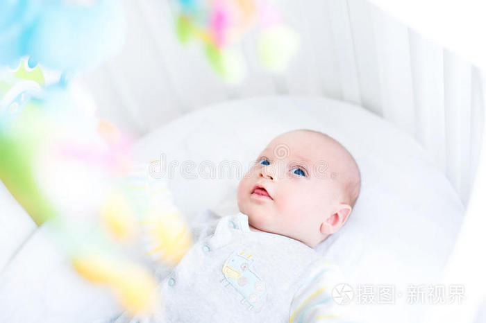 可爱的新生婴儿在他的白色婴儿床上看玩具