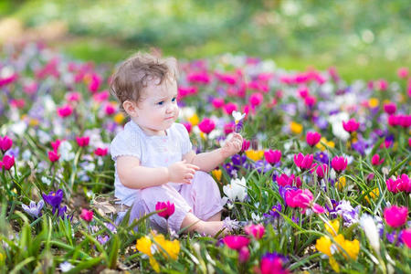 可爱的卷曲的小宝宝坐在春花之间