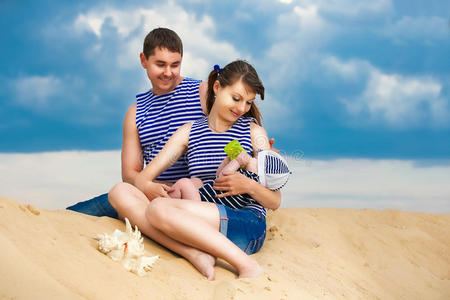 幸福的家庭，妈妈，爸爸，还有穿着条纹背心的小儿子在蓝天背景下的沙滩上玩得开心。夏天