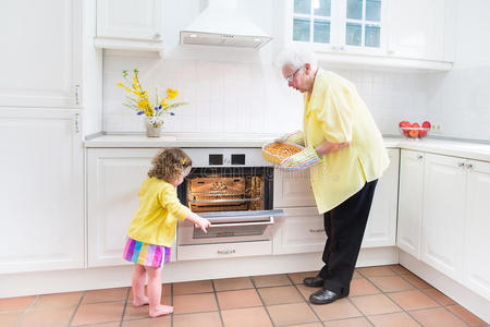 奶奶和可爱的女孩在白色的厨房里烤馅饼