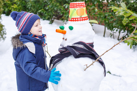 可爱的蹒跚学步的男孩堆雪人的乐趣在冬季的一天