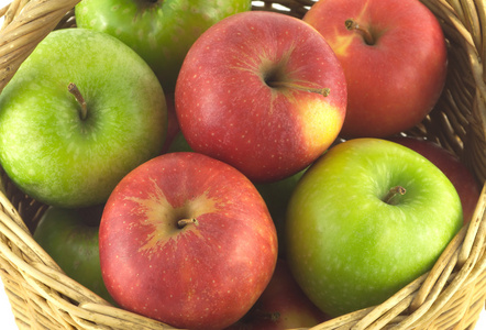 成熟的彩色苹果在孤立的棕色的柳条篮子里