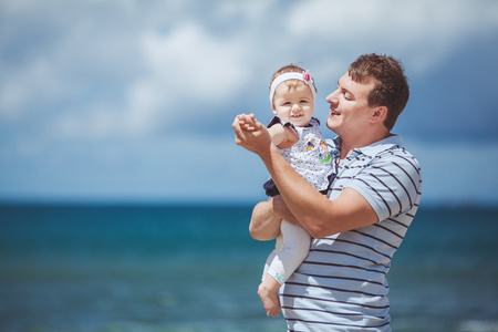 一个幸福的家庭的男人和婴儿儿童玩乐的蓝色的大海在夏季的肖像
