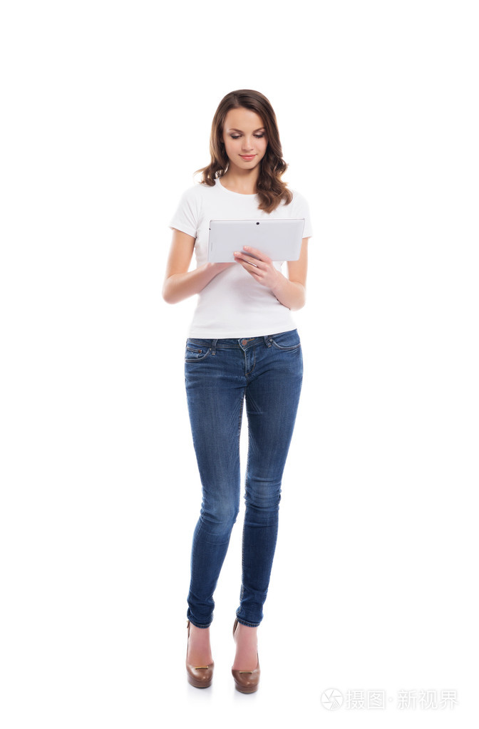 年轻快乐的女孩在时髦的牛仔裤，拿着平板电脑计算