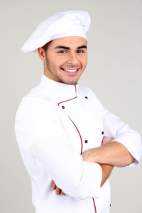 专业的厨师，在白色的制服和帽子，在灰色的背景上