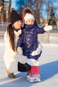 年轻的母亲和她可爱的小女儿在溜冰场上
