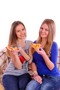 两个女孩坐在沙发上，一边吃比萨饼