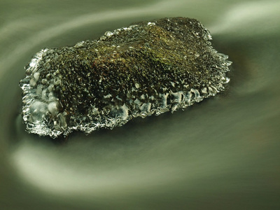 冻结在山区河流的黑暗冰冷的水中长满青苔的砂岩巨石。流奶模糊水面闪闪发亮的小冰柱