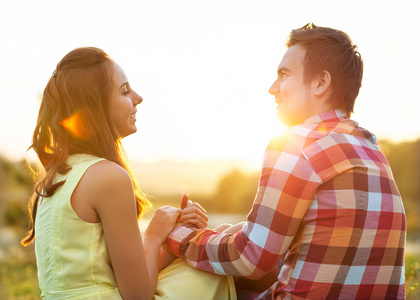 后视图的年轻幸福的夫妇，在日落时分坐在河上