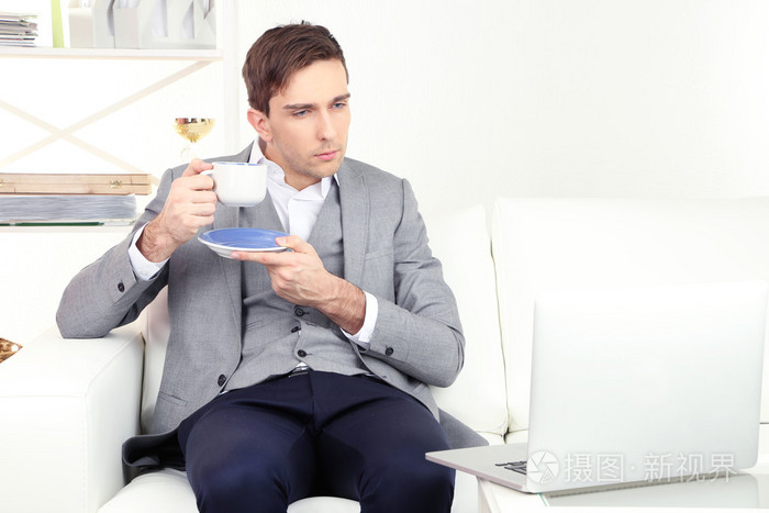 优雅的年轻商人坐在沙发上,和在家里喝咖啡