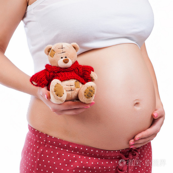 怀孕的母亲，显示她的肚子，抱着泰迪熊