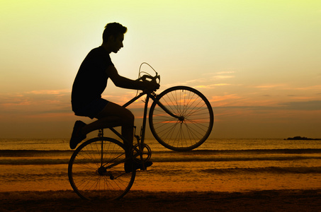 人在日出时在沙滩上，骑自行车健身在早上