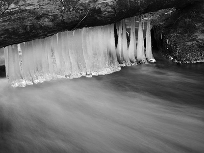 黑暗冰冷的水的山间溪流在冬天的时候，细细长长的冰柱垂挂乳白色水位以上