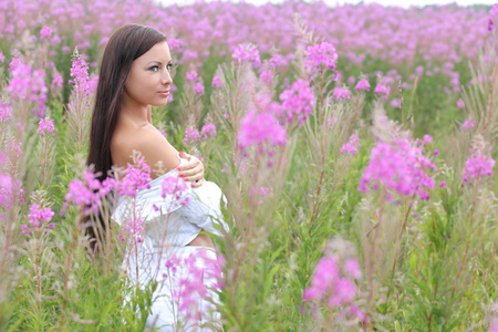 在高高的草丛背景上的白色连衣裙的年轻女子