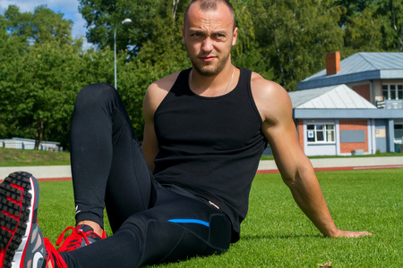 肌肉健壮的男子坐在体育场的草地上的形象